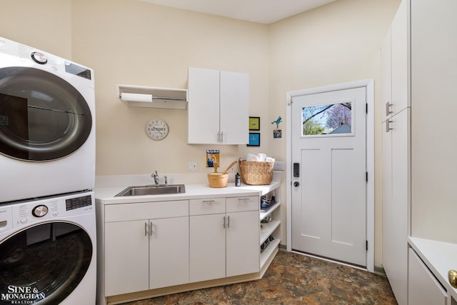 laundry room featuring stacked washer / dryer, stone finish floor, a sink, and cabinet space