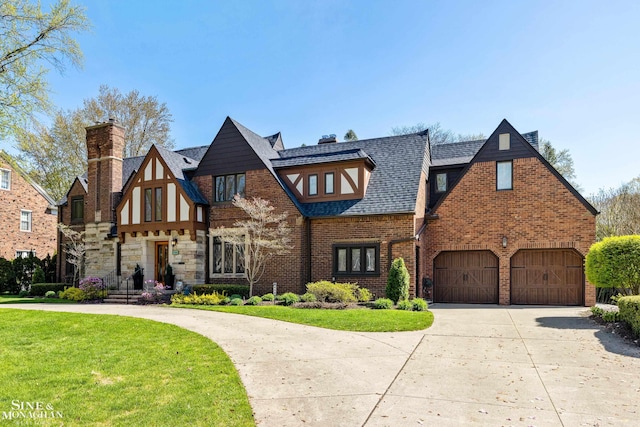 english style home featuring a chimney, driveway, brick siding, and a front yard
