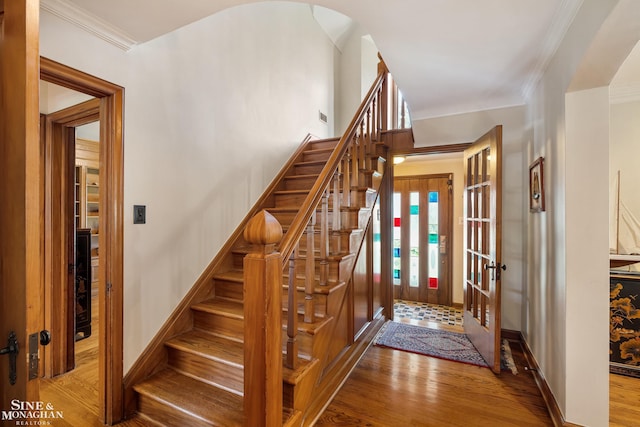 staircase featuring crown molding, arched walkways, baseboards, and wood finished floors