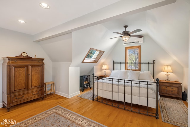 bedroom featuring light wood-style floors, a wall unit AC, a wood stove, and vaulted ceiling with skylight