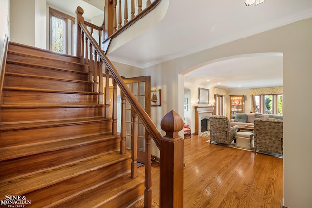 stairs with crown molding, arched walkways, and wood finished floors