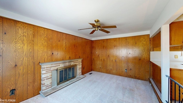 unfurnished living room with carpet floors, ceiling fan, wooden walls, and a fireplace