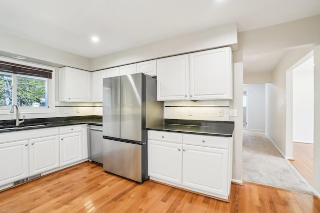 kitchen featuring dark countertops, a sink, light wood finished floors, stainless steel appliances, and white cabinetry