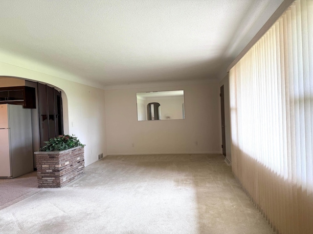 unfurnished living room featuring visible vents, arched walkways, a textured ceiling, and light carpet