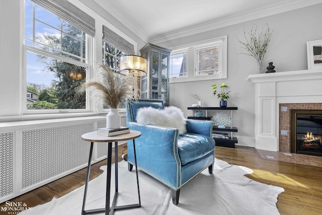 sitting room with a tiled fireplace, ornamental molding, radiator, and wood finished floors
