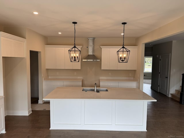 kitchen featuring a kitchen island with sink, wall chimney range hood, white cabinets, and a sink