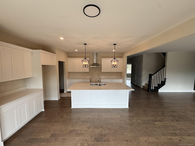 kitchen with a sink, wall chimney exhaust hood, a kitchen island with sink, white cabinetry, and baseboards