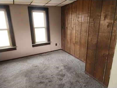 carpeted empty room with wood walls and a paneled ceiling