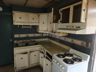 kitchen with a drop ceiling, range hood, white gas range, white cabinetry, and a sink