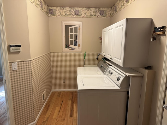 laundry room with light wood-style floors, wainscoting, cabinet space, and washer and clothes dryer