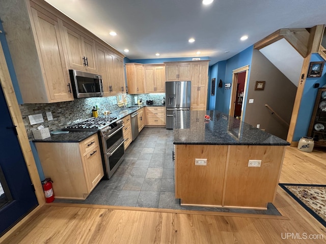kitchen with decorative backsplash, appliances with stainless steel finishes, a center island, wood finished floors, and dark stone counters