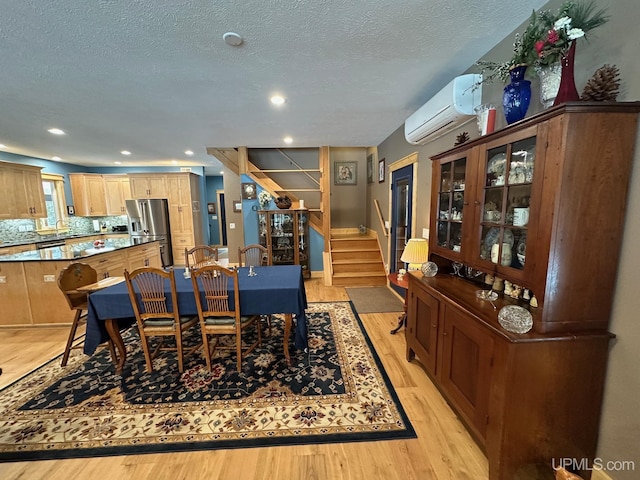 dining area featuring stairs, an AC wall unit, a textured ceiling, and light wood finished floors
