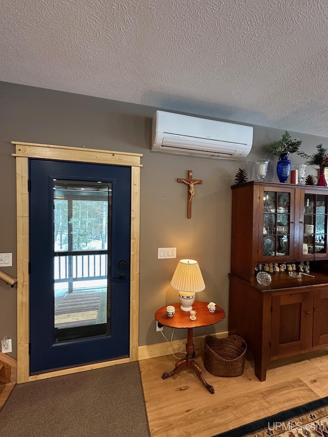 doorway with baseboards, a textured ceiling, a wall mounted AC, and wood finished floors