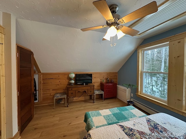 bedroom with light wood finished floors, wood walls, a ceiling fan, vaulted ceiling, and a baseboard heating unit