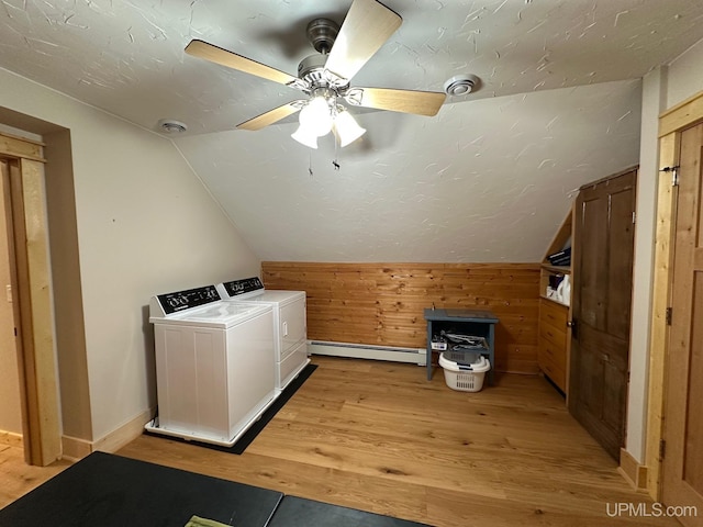 clothes washing area with a ceiling fan, independent washer and dryer, baseboard heating, wood walls, and light wood finished floors