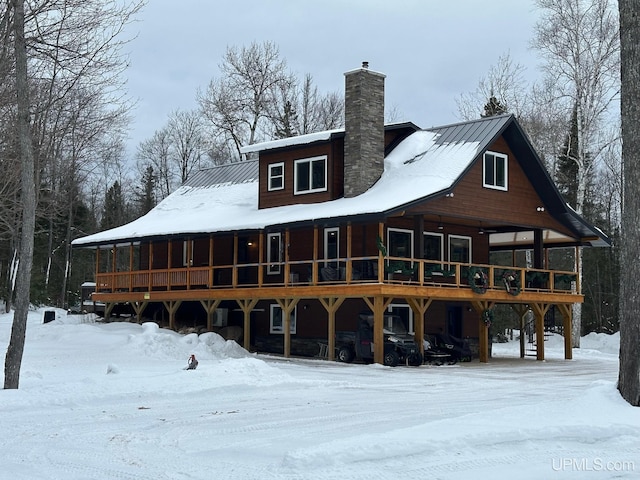 snow covered back of property featuring a chimney and metal roof