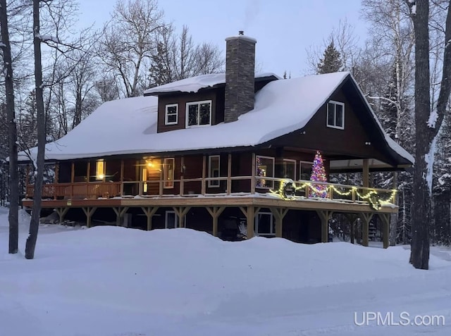 snow covered back of property featuring a deck and a chimney