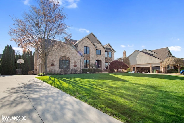french country home featuring stone siding, a front yard, brick siding, concrete driveway, and an attached garage