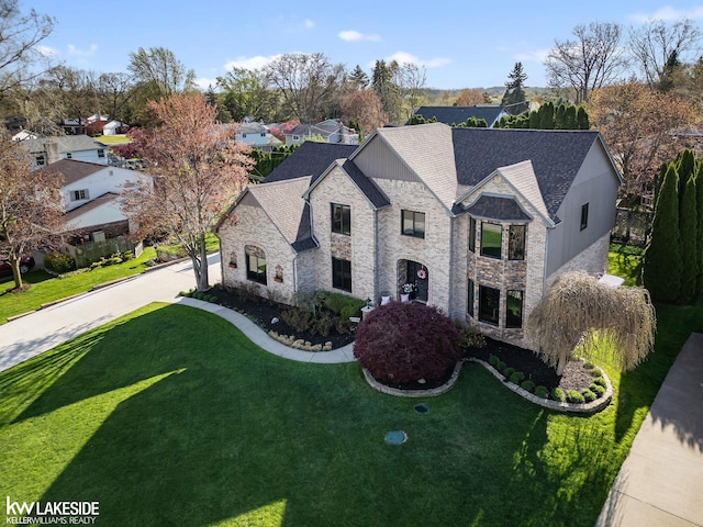 french country home with roof with shingles, stone siding, and a front lawn
