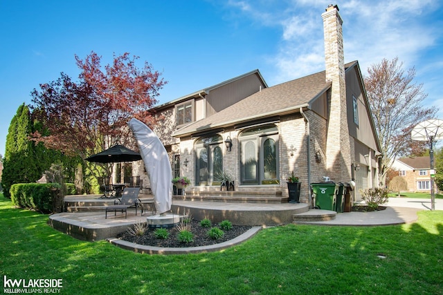 rear view of property with roof with shingles, brick siding, a chimney, a lawn, and a patio