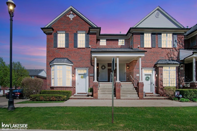 traditional home featuring brick siding, covered porch, and a front yard