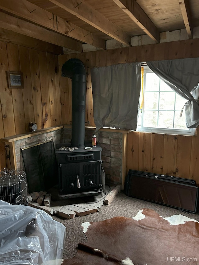 living area with carpet, beamed ceiling, a wood stove, and wood walls