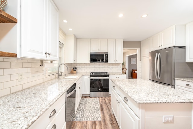 kitchen featuring decorative backsplash, a center island, a sink, stainless steel appliances, and white cabinetry