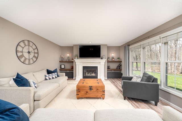 living area featuring baseboards, a tiled fireplace, and light wood finished floors