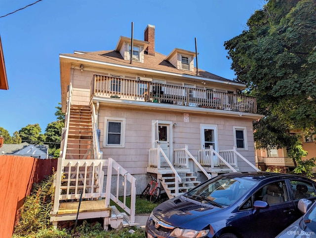 rear view of house featuring fence, a chimney, stairs, and a balcony