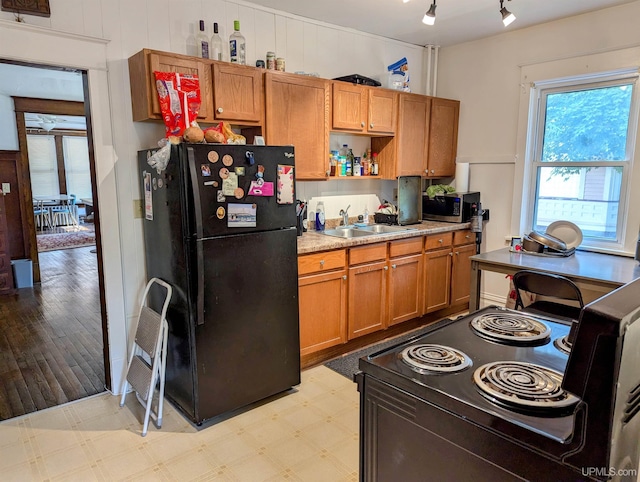 kitchen featuring open shelves, a sink, light countertops, brown cabinetry, and black appliances