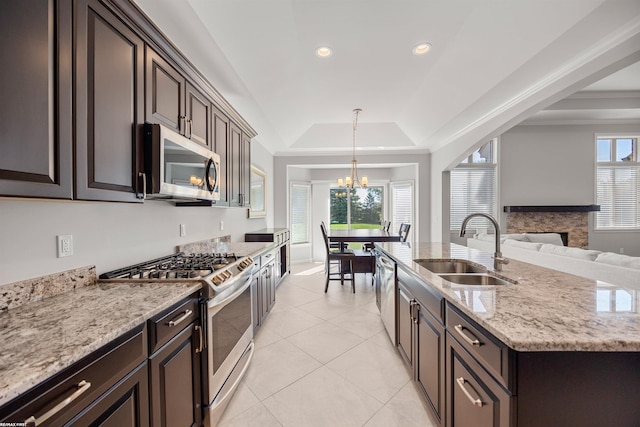 kitchen featuring appliances with stainless steel finishes, a fireplace, a sink, a chandelier, and a tray ceiling
