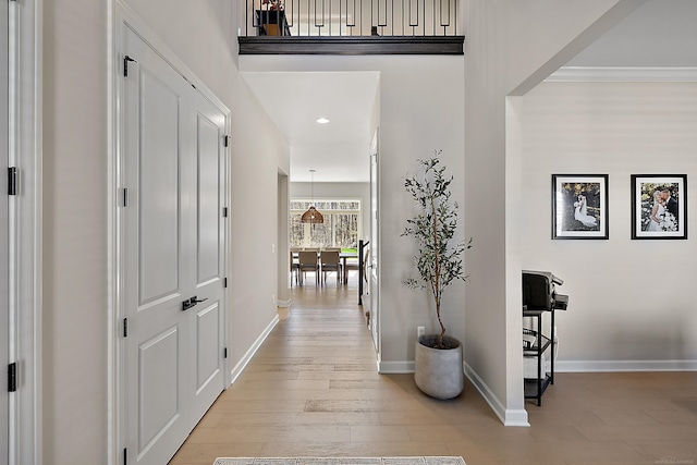 hallway with baseboards, recessed lighting, light wood-style flooring, and a high ceiling