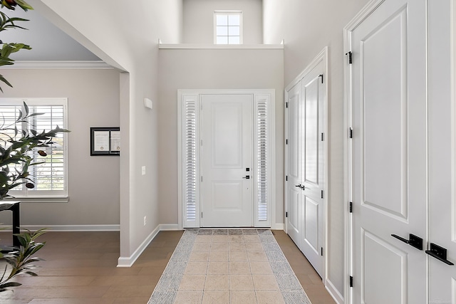 foyer entrance featuring baseboards, a high ceiling, crown molding, and wood finished floors