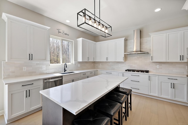 kitchen featuring gas cooktop, a sink, wall chimney exhaust hood, stainless steel dishwasher, and a kitchen island