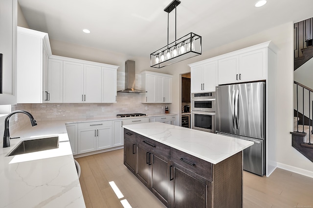 kitchen featuring a kitchen island, wall chimney range hood, a sink, appliances with stainless steel finishes, and backsplash