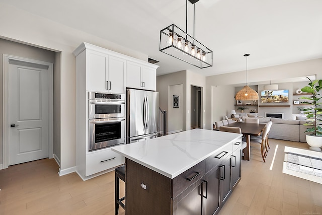 kitchen with decorative light fixtures, appliances with stainless steel finishes, a center island, light wood-type flooring, and white cabinets