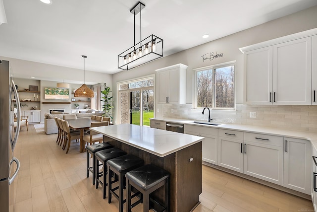 kitchen featuring open floor plan, light wood-type flooring, tasteful backsplash, a sink, and appliances with stainless steel finishes