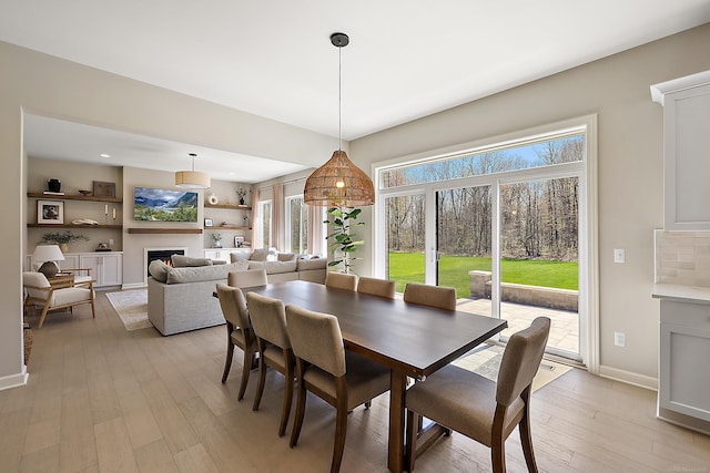 dining room featuring baseboards, light wood finished floors, and a warm lit fireplace