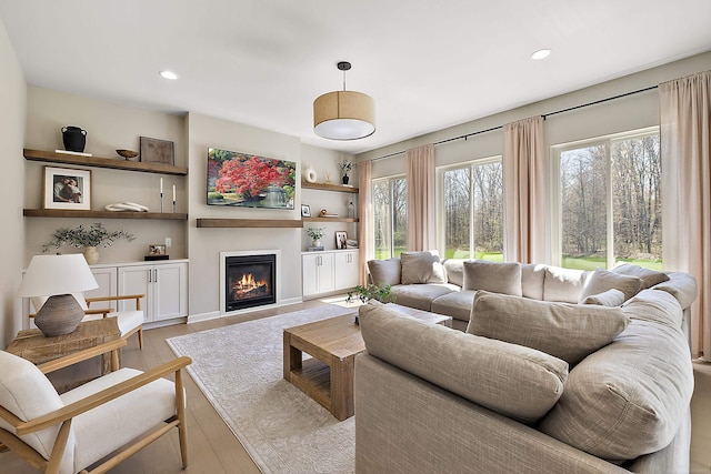 living room featuring light wood-style floors, a glass covered fireplace, and recessed lighting