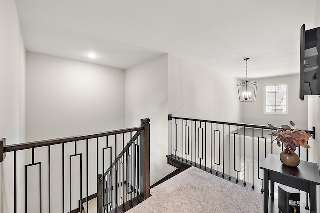 hallway featuring an inviting chandelier, carpet, and an upstairs landing