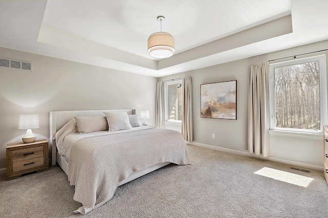 carpeted bedroom featuring visible vents, baseboards, and a tray ceiling