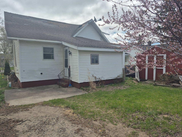 back of house featuring roof with shingles, an outdoor structure, entry steps, a patio, and a yard
