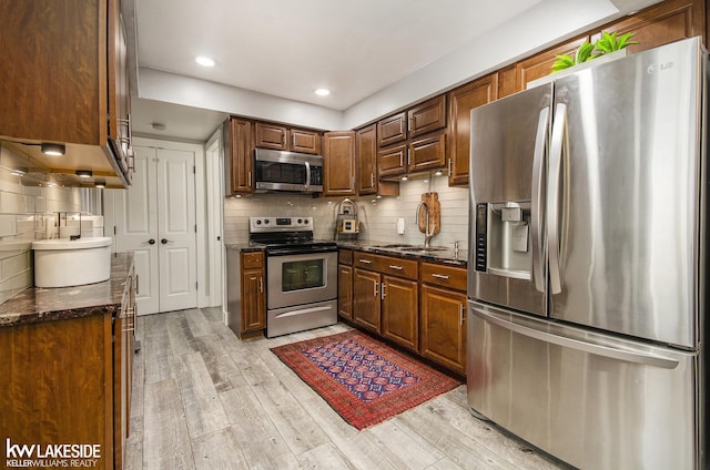 kitchen with backsplash, stainless steel appliances, a sink, and light wood-type flooring