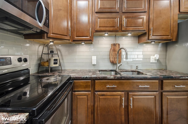 kitchen with backsplash, appliances with stainless steel finishes, a sink, and dark stone counters
