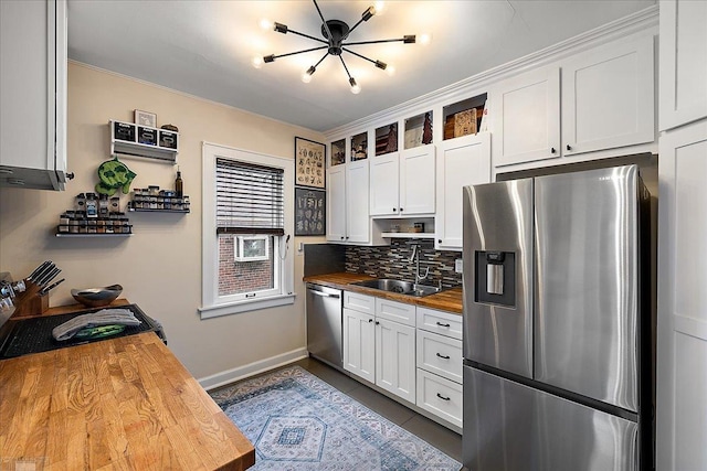 kitchen featuring butcher block counters, white cabinetry, a sink, appliances with stainless steel finishes, and backsplash