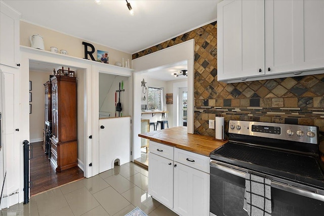 kitchen with white cabinets, tile patterned flooring, butcher block countertops, electric stove, and backsplash
