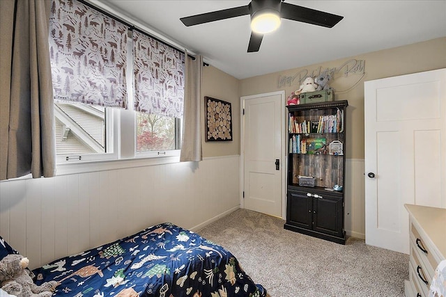 carpeted bedroom with wainscoting and ceiling fan