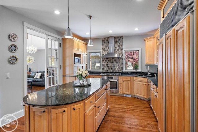 kitchen featuring wall chimney exhaust hood, stainless steel appliances, a healthy amount of sunlight, wood finished floors, and a kitchen island