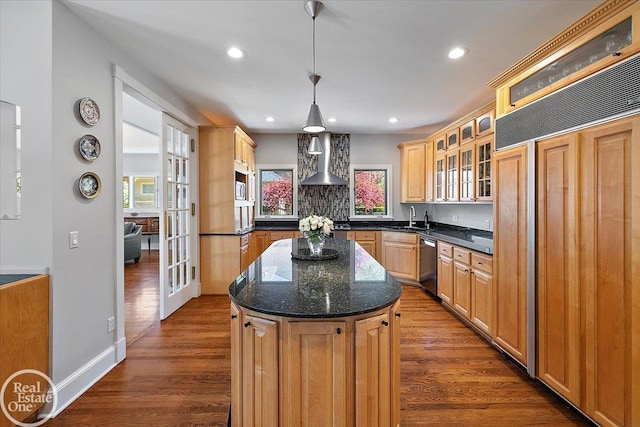 kitchen with appliances with stainless steel finishes, a center island, a sink, glass insert cabinets, and wall chimney exhaust hood