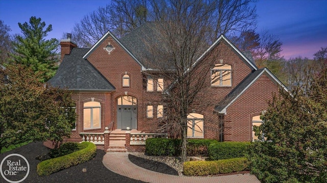 view of front of house with brick siding, a chimney, and a shingled roof